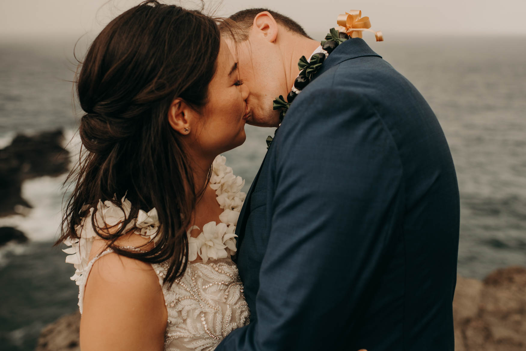 A slightly distant close-up of Andrew and Alison kissing with the grey-blue ocean out of focus in the background.