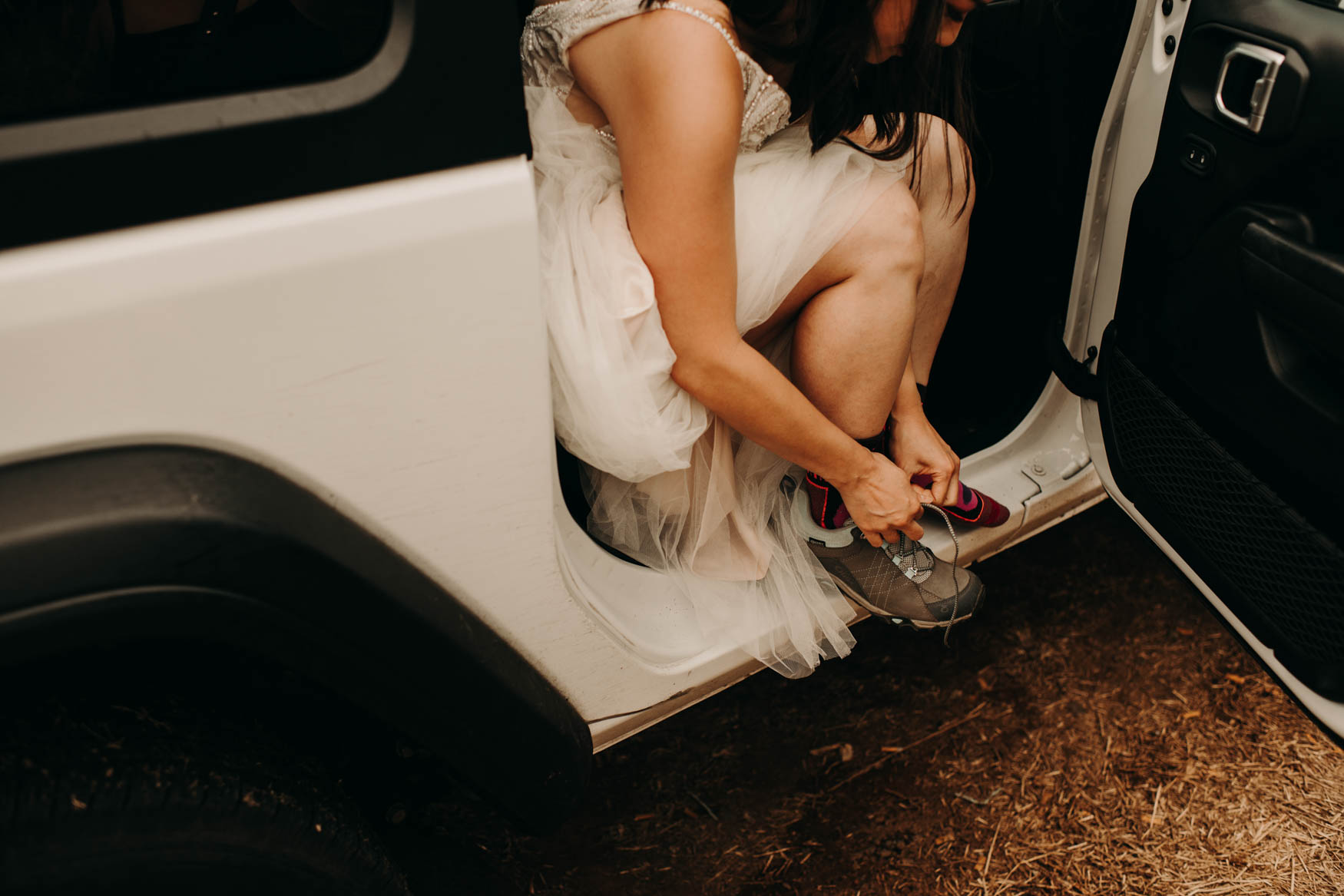 Alison, in her wedding dress, tying her hiking boots